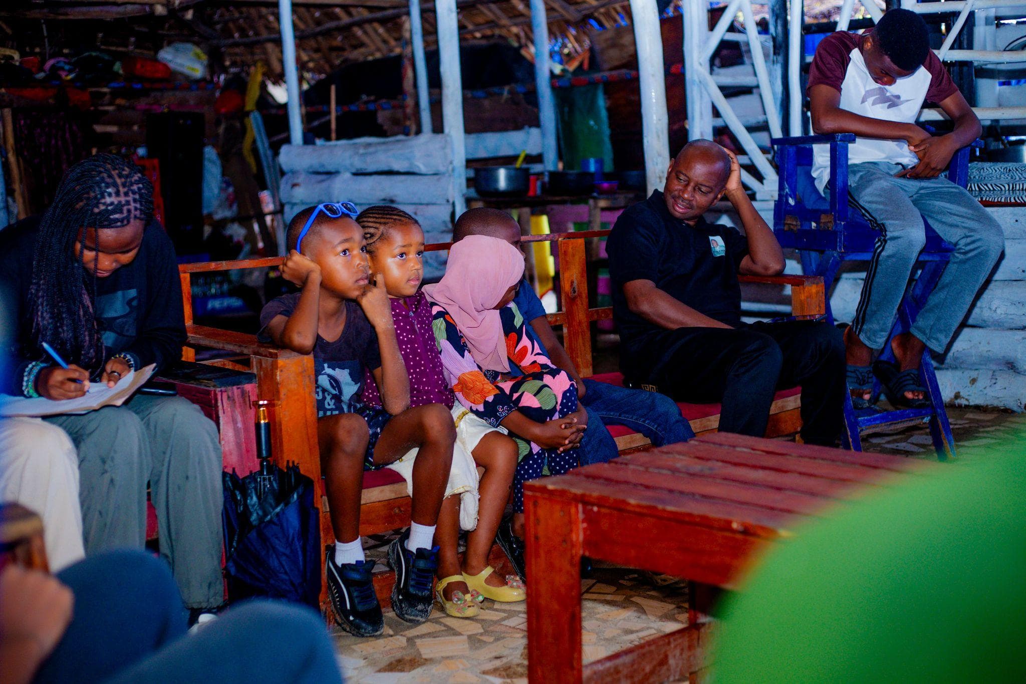 Young participants seated in the covered meeting space.
